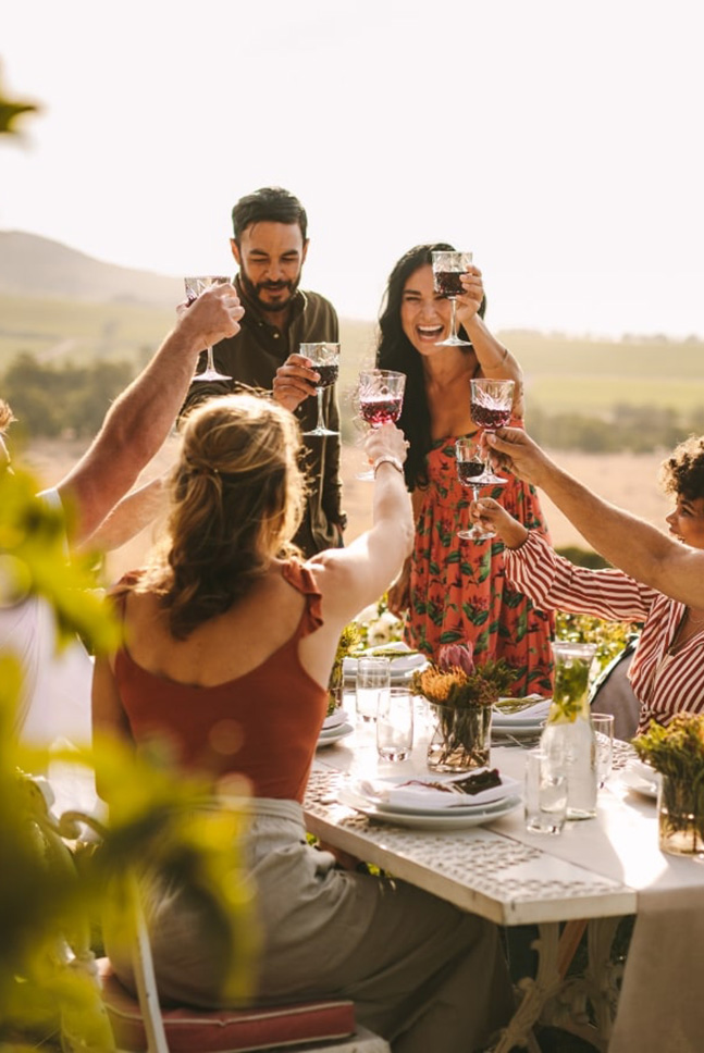 Eine Gruppe von Menschen prostet Wein an einem Tisch im Freien an.